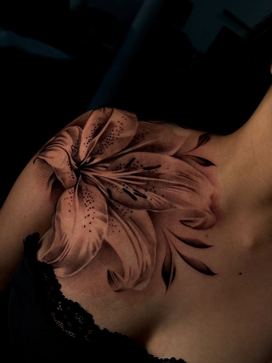 Photoreal black-and-grey lily across the shoulder and chest